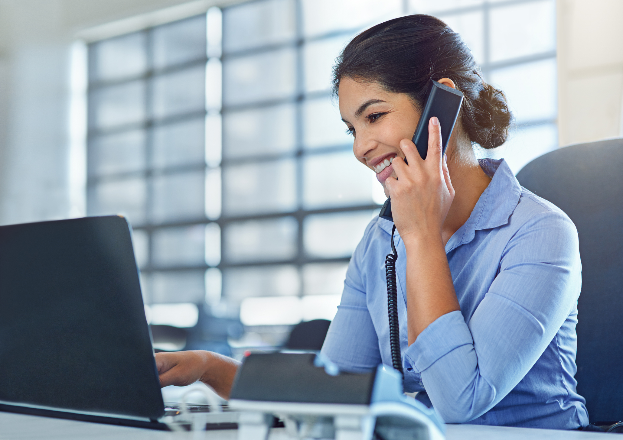 Young businesswoman talking on the phone while using a laptop at work