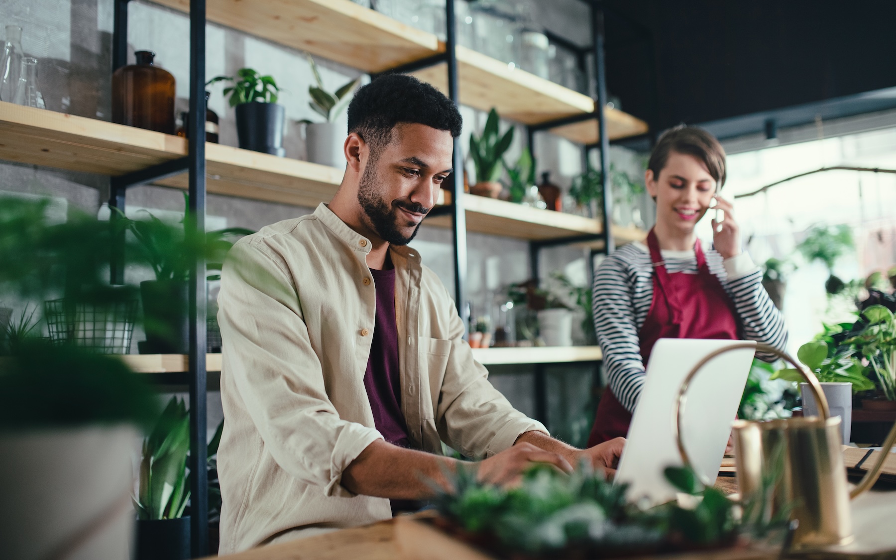 Man using devices for online business order at bakehouse Man and woman shop assistants with laptop working in indoor potted plant store, small business concept.