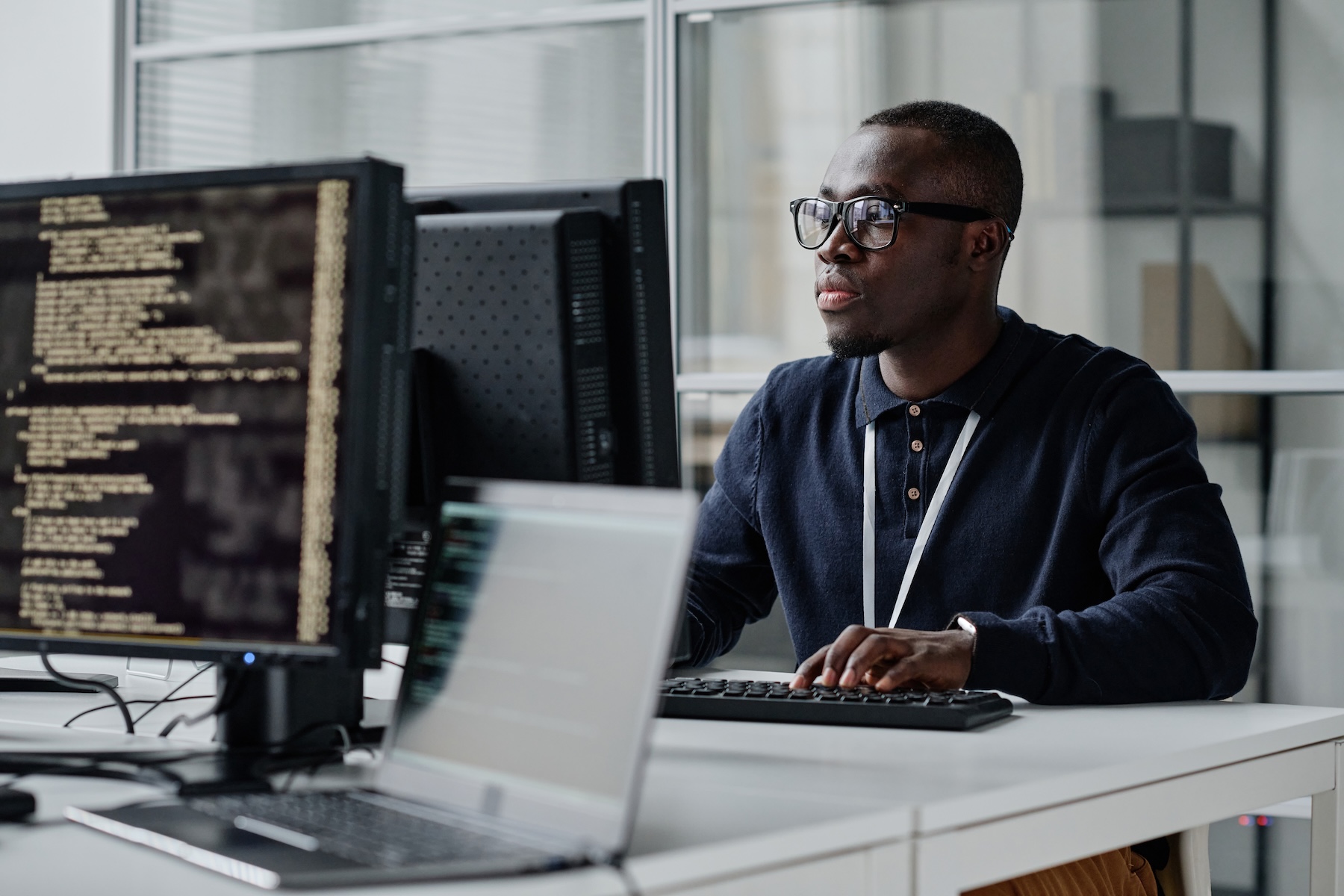 Young African American developer with glasses concentrating on his online work on workplace computer